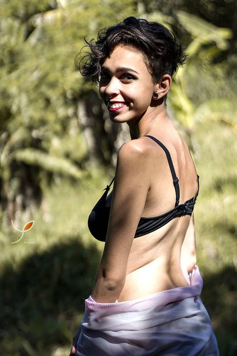 Nesta foto sensual a modelo está com um sutiã preto, num campo e olhando para trás - mostrando um sorriso para o fotógrafo.'