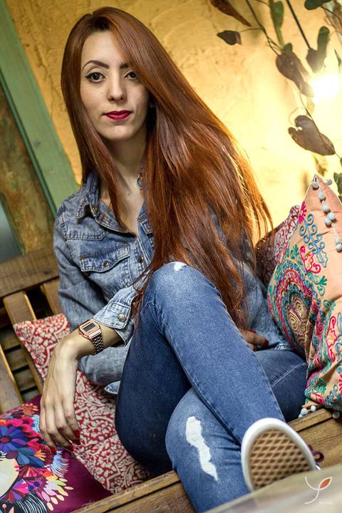 Modelo ruiva usando roupas jeans sentada num banco com almofadas de uma cafeteria de São José dos Campos e olhando para a câmera.  '