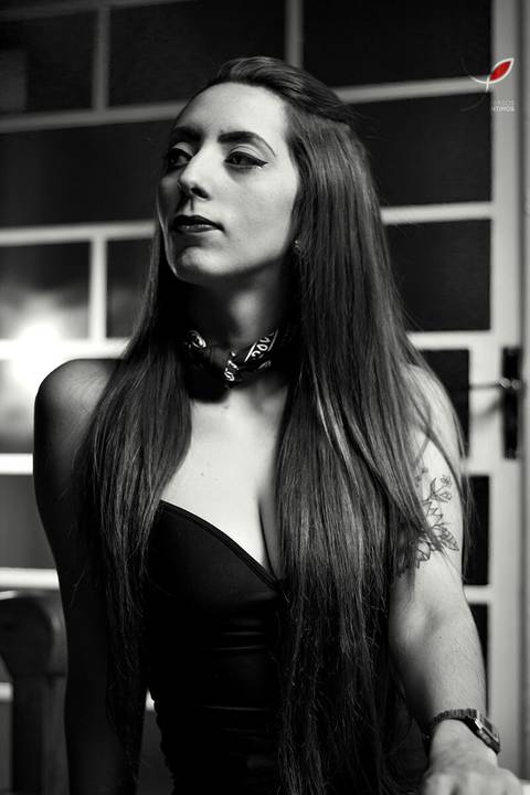 Fotografia em preto e branco da modelo sentada na mesa de uma cafeteria. Ela veste uma camisa preta e tem tatuagem nos braços. Na imagem ela olha para o lado.'