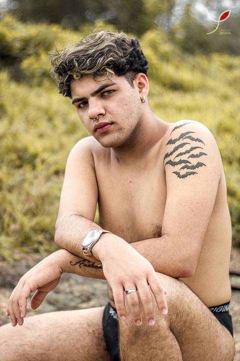 O modelo branco, de cueca e sem camiseta, está sentado numa pedra e olhando para a câmera.'