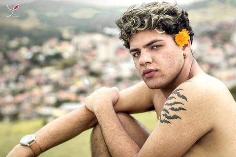 O modelo branco, de cueca e sem camiseta, está sentado numa pedra e olhando para a câmera. Com a cidade no fundo.'