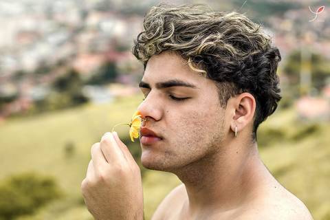 O modelo branco, de cueca e sem camiseta, está sentado numa pedra e olhando para a câmera. Com a cidade no fundo.'