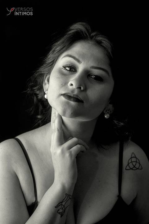 Modelo com tatuagens e vestido preto posando em uma fotografia de estúdio. Ela olha para a câmera nesta fotografia em preto e branco.'