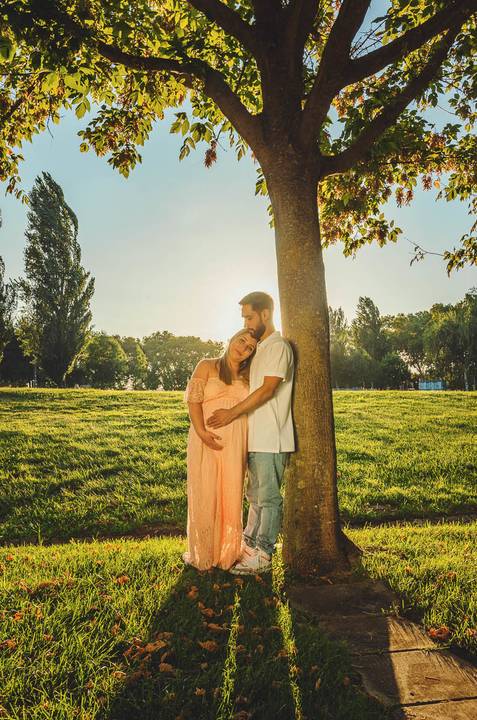 Casal sob árvore com gestante em pose aconchegante'