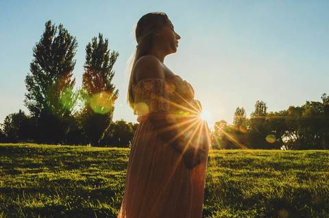 Mulher grávida em pé com luz do entardecer dourada '