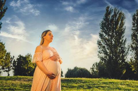 Mulher grávida em amarelo com mãos na barriga redonda'