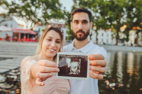 Casal em parque com mulher grávida em centro da foto'