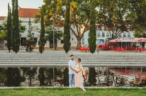 Casal em parque verde com mulher grávida sorrindo radiante'