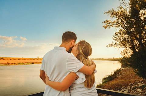 Mulher grávida de pôr do sol ao fundo com expressão de felicidade'