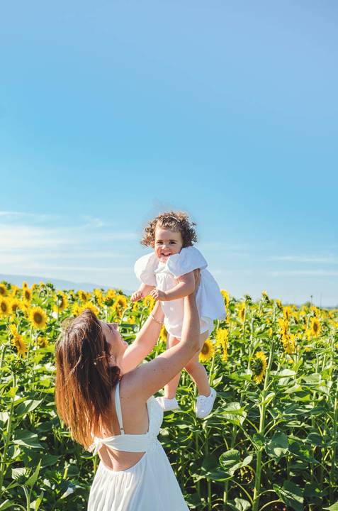 Criança pequena em retrato individual durante sessão fotográfica em campo de girassóis. Menina brincando em ambiente rural com foco em expressão alegre. Fotografia artística capturando beleza infantil em composição natural descontraída.'