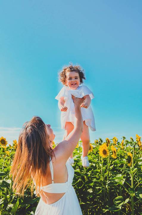 Menina em retrato individual em sessão familiar em campo de girassóis ao céu azul. Criança brincando em ambiente natural com foco em rosto e expressão. Fotografia profissional capturando alegria e inocência infantil em composição artística cuidadosa.'