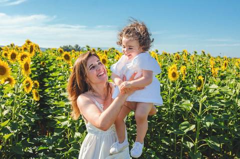Menina pequena em retrato individual em campo de girassóis ao céu azul. Criança brincando em sessão familiar profissional ao ar livre. Fotografia artística capturando expressão alegre e natural de criança em ambiente rural.'