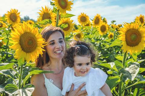 Menina em retrato individual em sessão familiar em campo abundante de girassóis. Criança brincando em ambiente natural rural com céu azul ao fundo. Fotografia profissional capturando beleza infantil em composição artística descontraída.'
