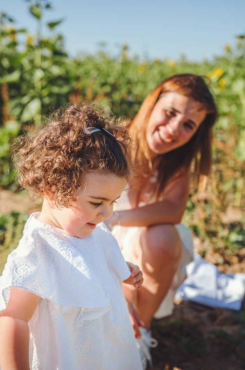 Criança pequena em retrato individual em sessão familiar brincando em ambiente natural. Menina sorridente em campo com girassóis ao fundo durante fotografia ao ar livre. Fotografia profissional capturando alegria e inocência infantil.'