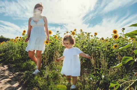 Mulher adulta e criança pequena em retrato em sessão familiar em campo natural. Mãe segurando filha entre girassóis durante fotografia ao ar livre. Fotografia profissional capturando momentos familiares emocionales em ambiente rural paisagístico.'