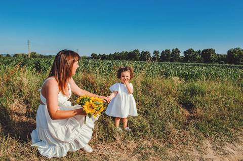 Mulher adulta segurando criança em retrato familiar em sessão ao ar livre em campo. Mãe segurando filha pequena em ambiente rural natural de paisagem aberta. Fotografia profissional capturando momento emocional familiar em composição artística.'
