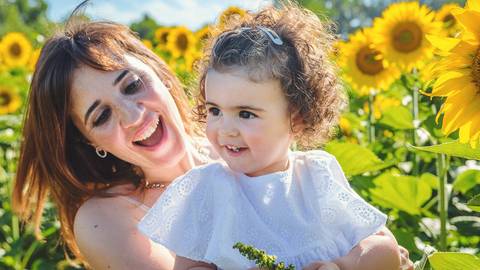 Menina em retrato individual rodeada de girassóis amarelos vibrantes em sessão ao ar livre. Criança brincando em ambiente rural natural com foco em expressão facial joyosa. Fotografia profissional capturando beleza infantil em composição artística.'