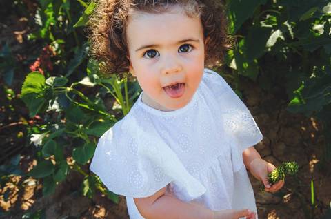 Menina em retrato naturalista em sessão fotográfica profissional ao ar livre em campo rural. Criança brincando em ambiente natural com foco em expressão facial alegre. Fotografia artística capturando inocência infantil em composição delicada e emocional.'