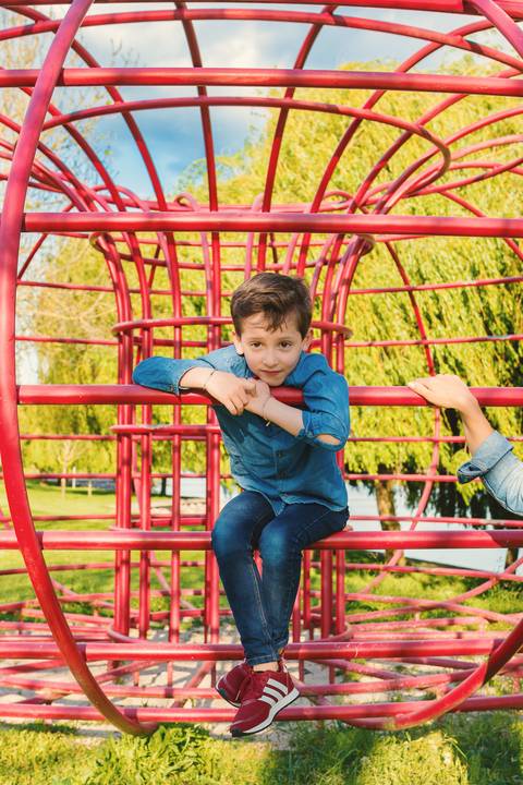 Menino brincando em estrutura vermelha no parque'