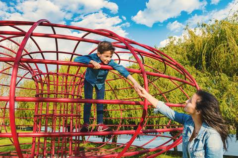 Menino se pendurado em estrutura de parque com sorriso'