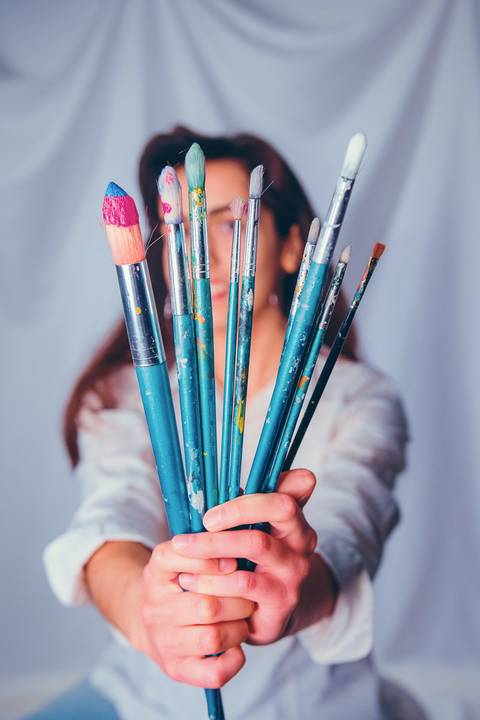 Detalhe de mãos com pincéis de pintura artística colorida'