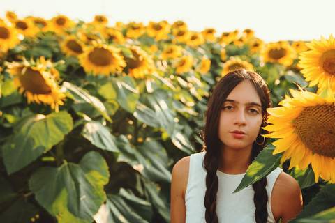 Mulher entre girassóis segurando flor amarela com luz natural'