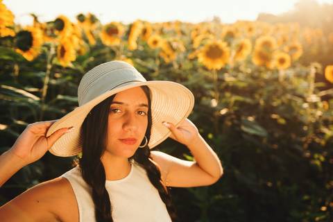 Mulher com chapéu branco em meio aos girassóis durante golden hour'