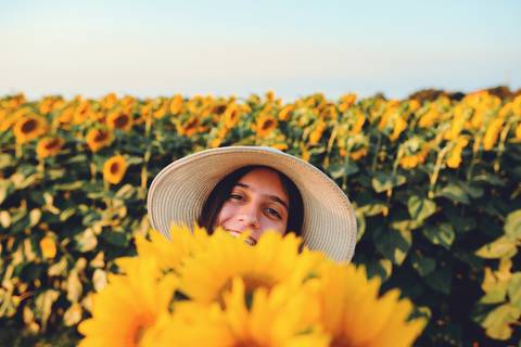 Mulher com chapéu e girassóis amarelos em ambiente natural'