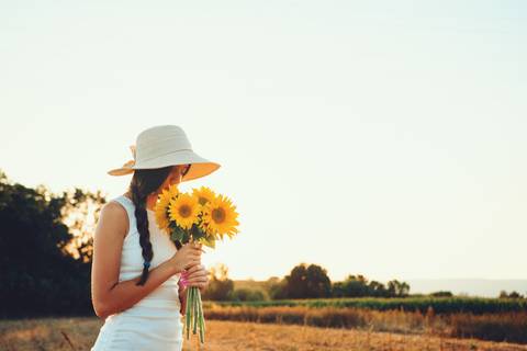 Mulher com chapéu branco contemplando paisagem rural de girassóis'