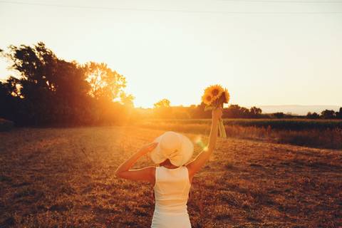 Mulher em vestido branco com girassol ao pôr do sol no campo'