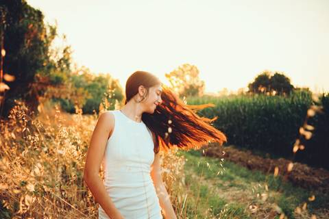 Mulher em vestido branco cercada de girassóis com sol radiante ao fundo'