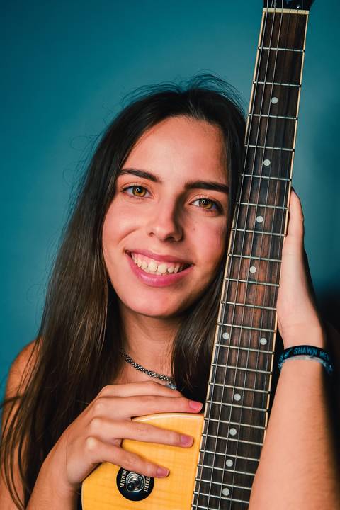 Mulher abraçando violão com sorrisosorridente em estúdio azul'