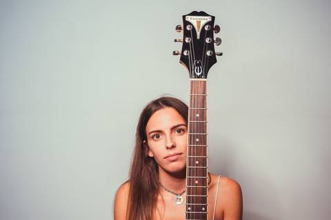 Mulher segurando violão em estúdio com fundo cinza neutro'