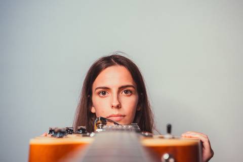 Mulher com violão olhando para frente em estúdio neutro'