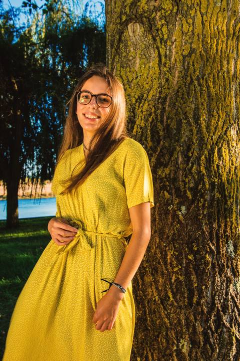 Mulher com violão e vestido amarelo junto a árvore no parque'