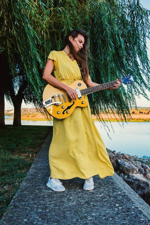 Mulher com violão em vestido amarelo em parque arborizado'