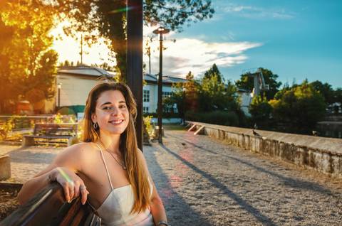 Mulher apoiada em muro de pedra com pôr do sol ao fundo'