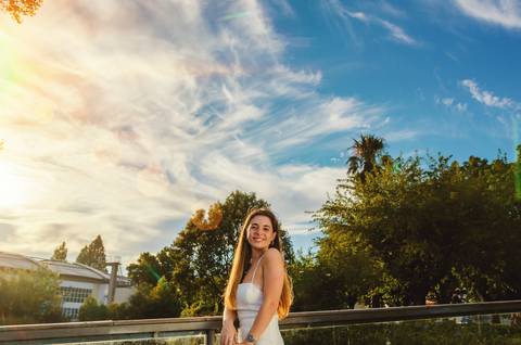 Retrato feminino em jardim com vegetação e céu azul ao fundo'