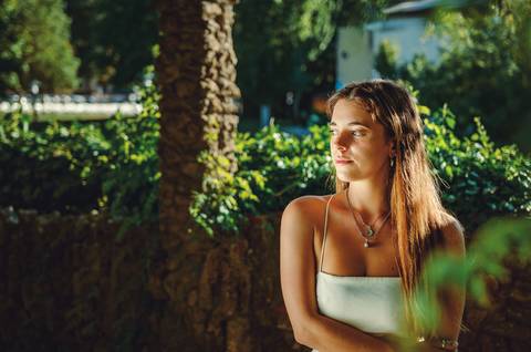 Mulher em vestido branco próxima a tronco de árvore com luz solar'