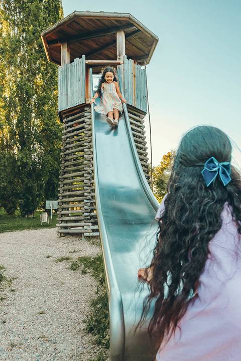 Família completa posando unida em parque natural com árvores ao fundo, retrato intergeracional com pais, filhas e criança, sessão fotográfica outdoor com luz golden hour ao pôr do sol'