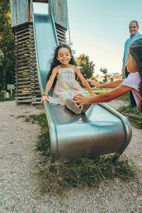 Menina posando em frente a estrutura de madeira em parque, retrato infantil individual durante sessão fotográfica de família, criança sorrindo com luz natural ao entardecer'