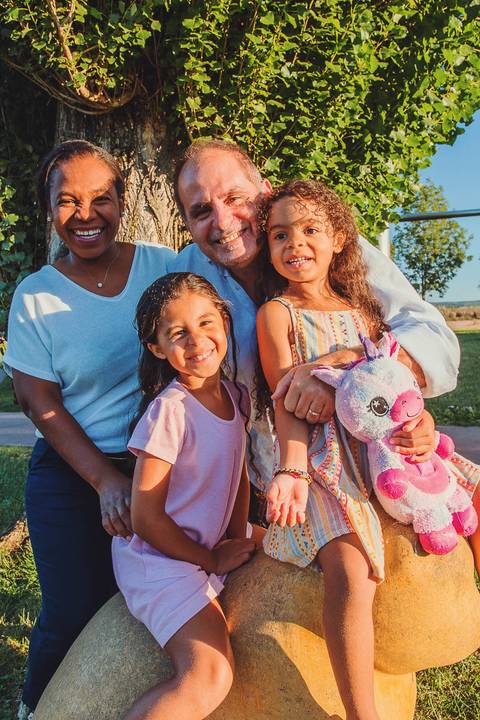 Pais e filhas abraçadas durante sessão fotográfica de família em ambiente externo, momento lifestyle caloroso e genuíno com crianças alegres, Barquinha Parque ao pôr do sol'