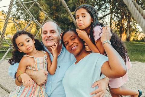 Mãe com duas filhas posando unidas em ambiente de parque com grama verde, retrato familiar com abraço de mãe e filhos ao ar livre, sessão fotográfica lifestyle com luz natural ao pôr do sol'
