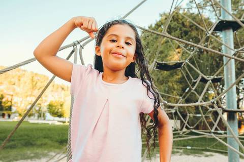 Menina em close posando com olhar para câmera durante sessão fotográfica ao ar livre, retrato infantil individual com luz dourada ao entardecer, fotografia de criança em ambiente natural'