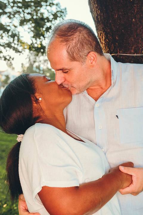 Casal abraçado e se beijando durante sessão fotográfica de família em parque ao pôr do sol, retrato romântico com abraço íntimo de cônjuges com luz golden hour dourada natural'