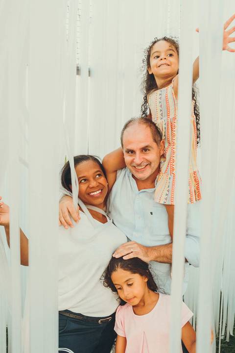 Família completa abraçada durante sessão fotográfica ao caminhar em parque ao entardecer, retrato familiar ao ar livre com pais e filhas unidas com luz golden hour natural'