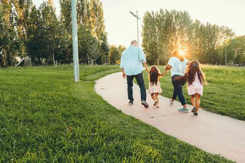 Família caminhando em trilha de parque ao entardecer durante sessão fotográfica, retrato familiar ao ar livre em caminho com grama e árvores com luz golden hour'
