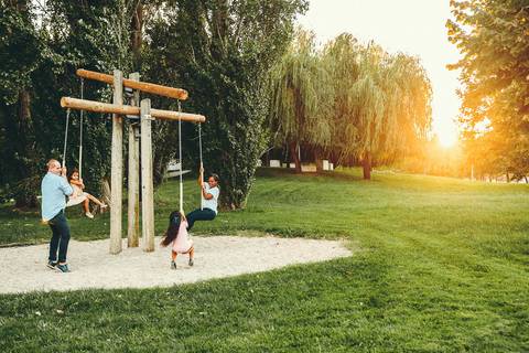 Menina em estrutura vermelha de parque ao entardecer durante sessão fotográfica, retrato infantil brincando em equipamento de lazer ao ar livre com luz golden hour natural'