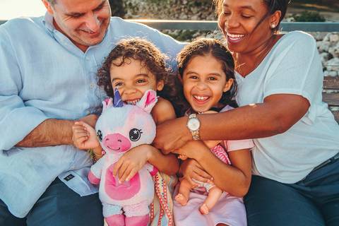 Pai com filhas pequenas em close, momento familiar caloroso durante sessão fotográfica, conexão de pais e filhos retratada com intimidade e carinho, fotografia de família profissional'
