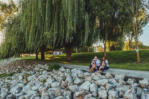 Família reunida em ambiente de parque com árvores grandes, sessão fotográfica de família com luz natural ao entardecer, retrato generations com pais, filhas e criança ao ar livre'